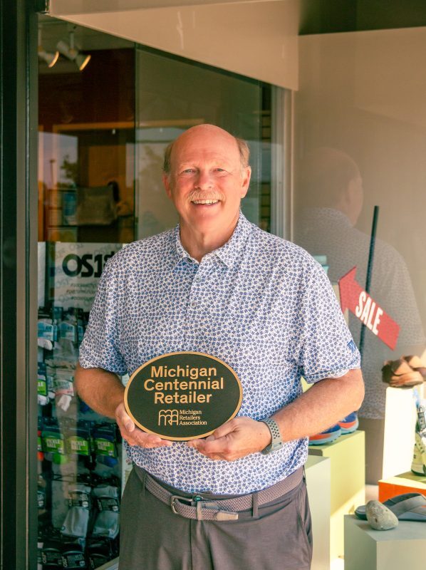 man holding up michigan centennial retailer plaque