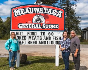Cort, Pam and Ken Sandy pose in front of the Meauwataka General Store sign